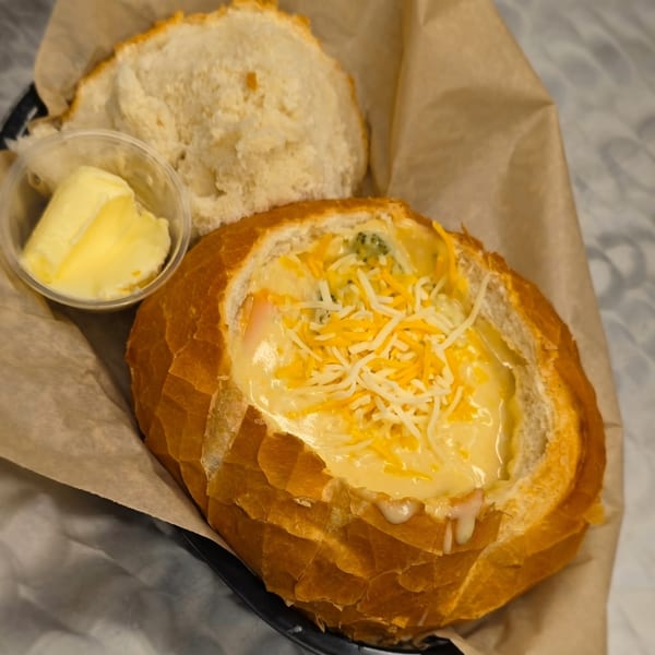 Creamy soup in a bread bowl topped with shredded cheese, served with a side of butter.