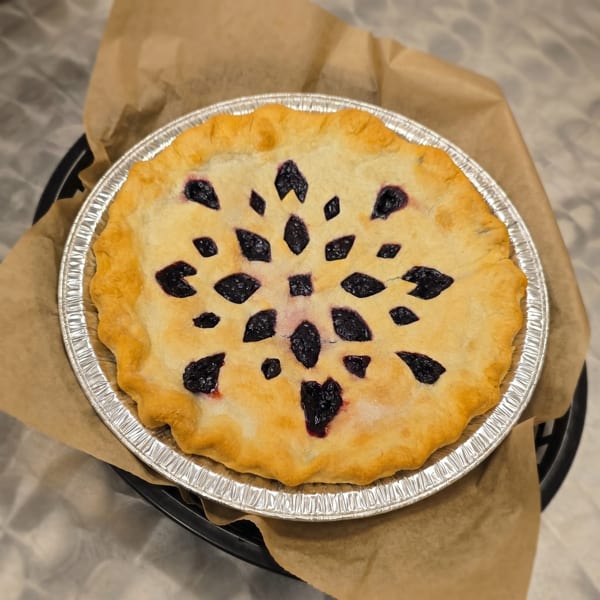 A freshly baked blueberry pie with a decorative snowflake crust design in a foil pan.