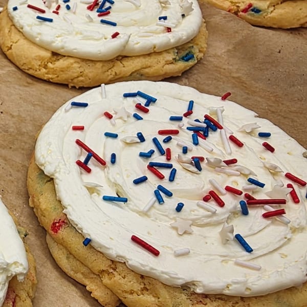 Sugar cookies with white frosting and red, white, and blue sprinkles on parchment paper.